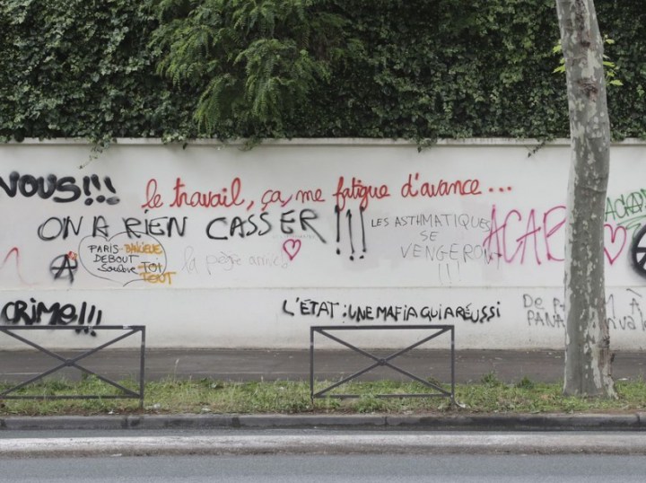 People stand on June 15, 2016 near graffiti, spray painted during a demonstration against labour reforms on June 14, covering a wall on Boulevard des Invalides in Paris. / AFP PHOTO / Jacques DEMARTHON