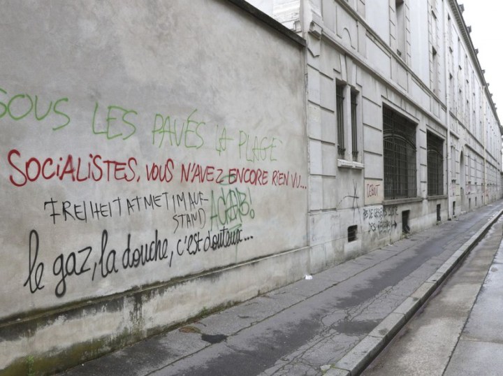 A woman walks on June 15, 2016 past graffiti, spray painted during a demonstration against labour reforms on June 14, reading "Socialists, you haven't seen anything yet..." (L) near Victor Duruy high school on Boulevard des Invalides in Paris. / AFP PHOTO / Jacques DEMARTHON